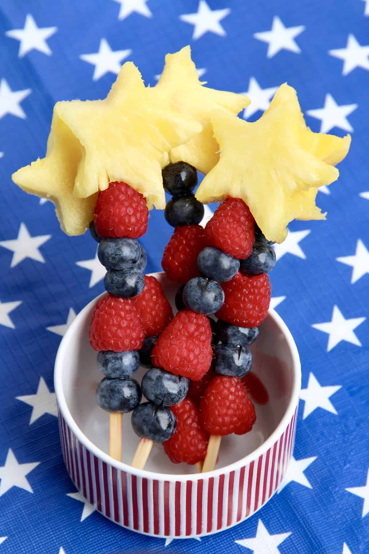 Star shaped pineapple pieces, raspberries and blueberries on a cocktail skewer.