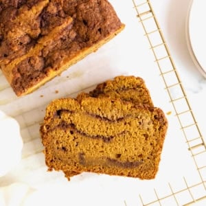 Sliced cinnamon swirled pumpkin bread on a parchment lined, gold tone cooling rack.