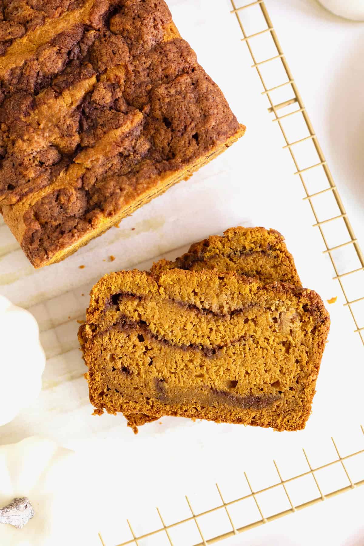 Sliced cinnamon swirled pumpkin bread on a parchment lined, gold tone cooling rack.