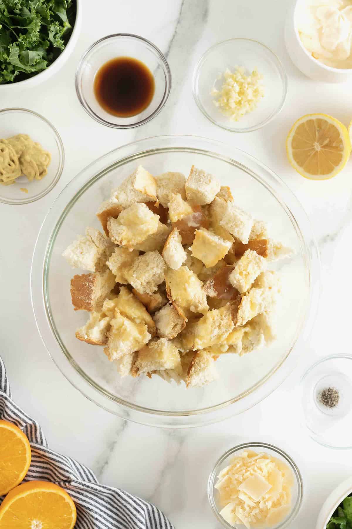 Cubed bread in a large glass mixing bowl tossed with spices.