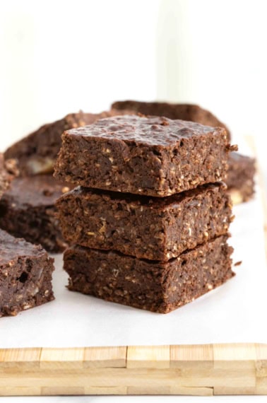 A stack of three breakfast brownies on a parchment lined wooden cutting board.