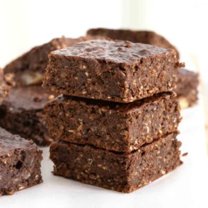 A stack of three breakfast brownies on a parchment lined wooden cutting board.