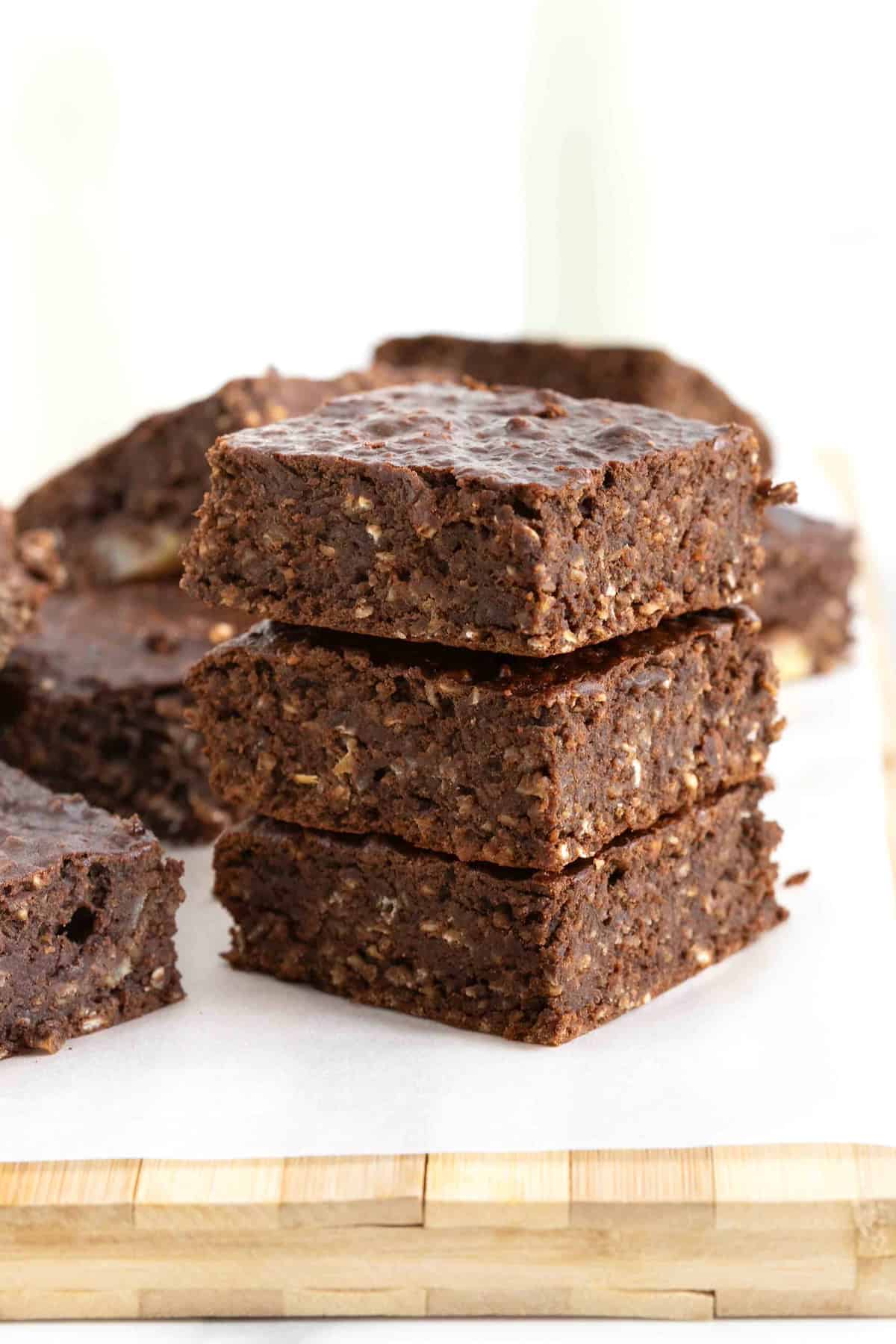 A stack of three breakfast brownies on a parchment lined wooden cutting board.