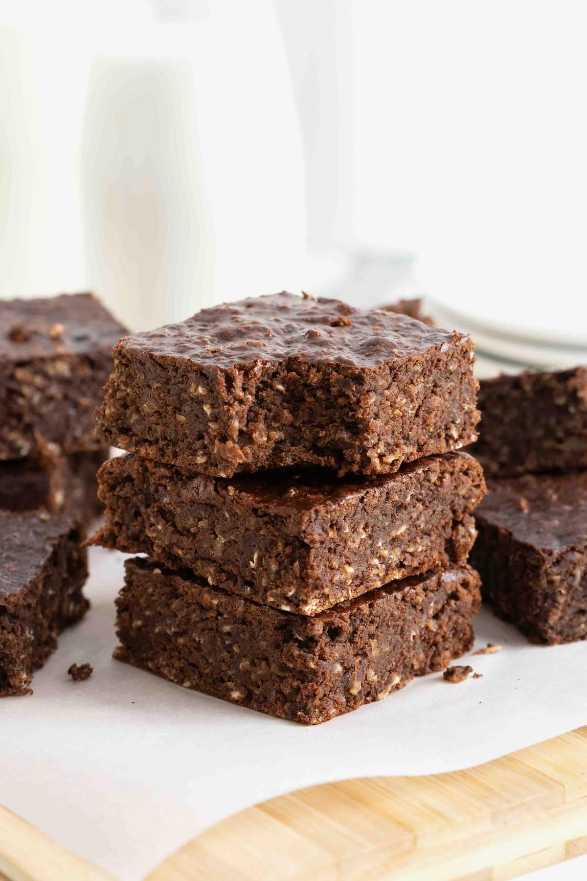 A stack of three breakfast brownies on a parchment lined wooden cutting board. The top brownie has a bite out of it.