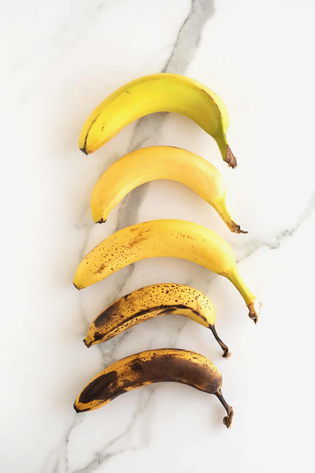 Bananas of varying ripeness on a white marble counter.