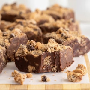 Several pieces of chocolate chip cookie fudge on a parchment lined surface.