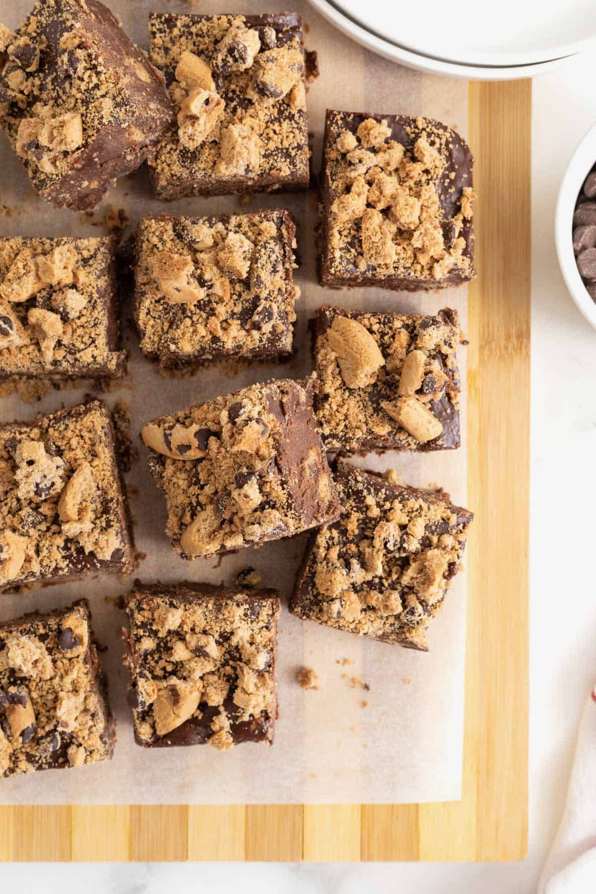 12 squares of chocolate chip cookie fudge on a parchment lined light wood cutting board.