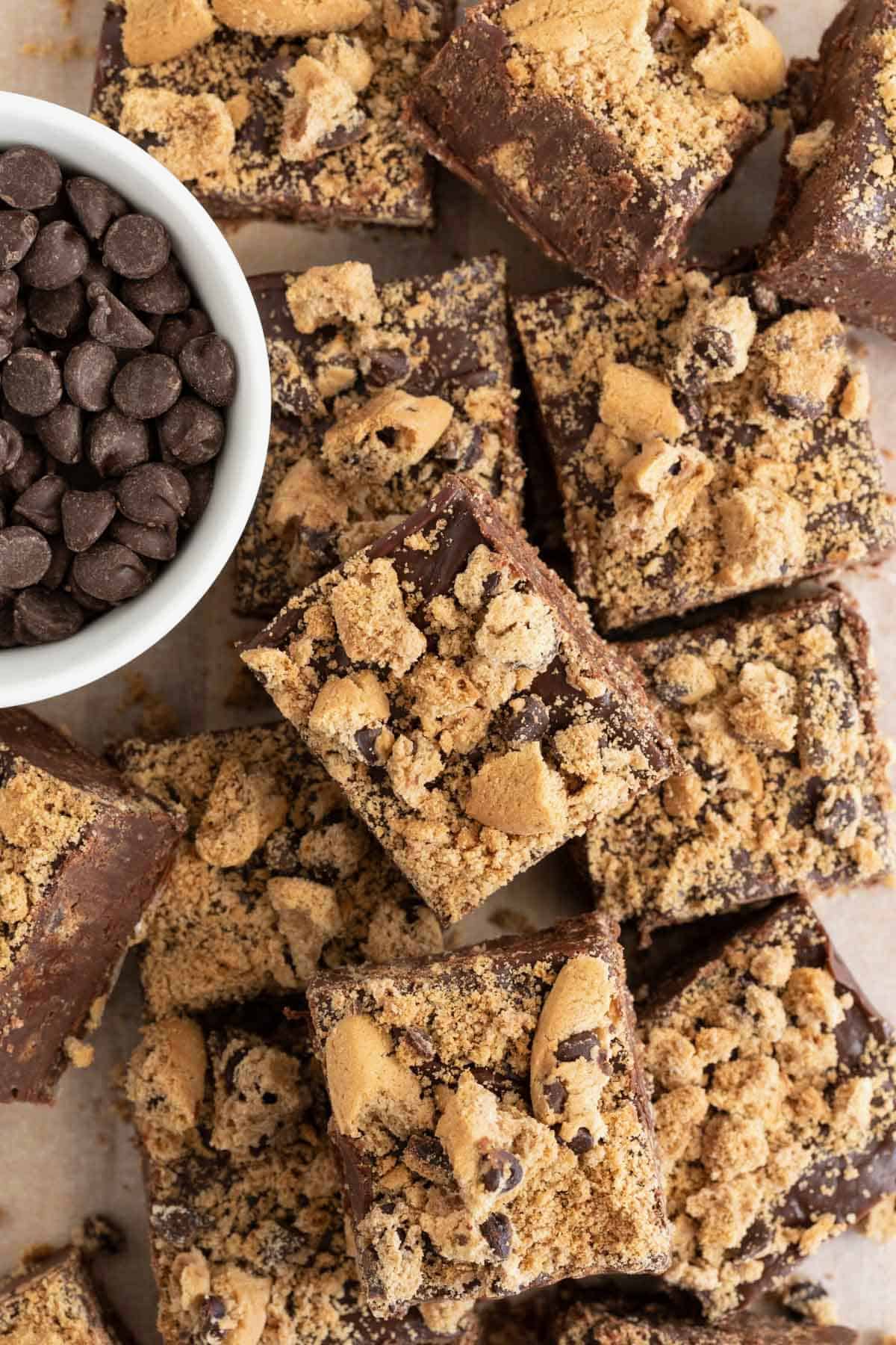 A pile of fudge squares next to a small white dish of chocolate chips.
