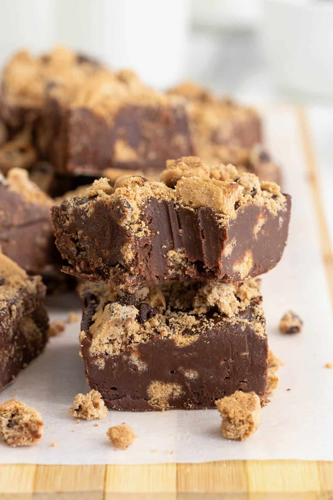 Chocolate fudge with chocolate chip cookies embedded in it on a parchment lined wooden cutting board.