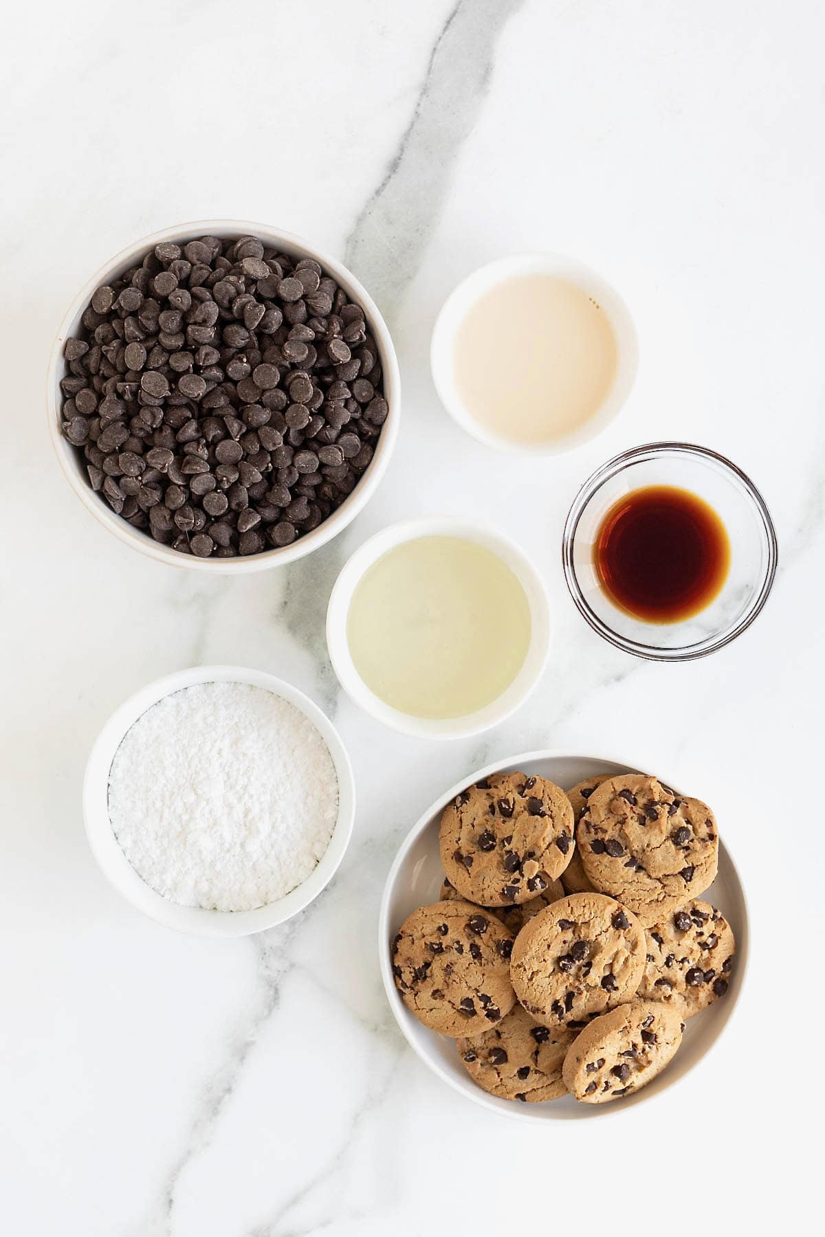 Ingredients to make chocolate chip cookie fudge in small glass dishes on a white marble counter.