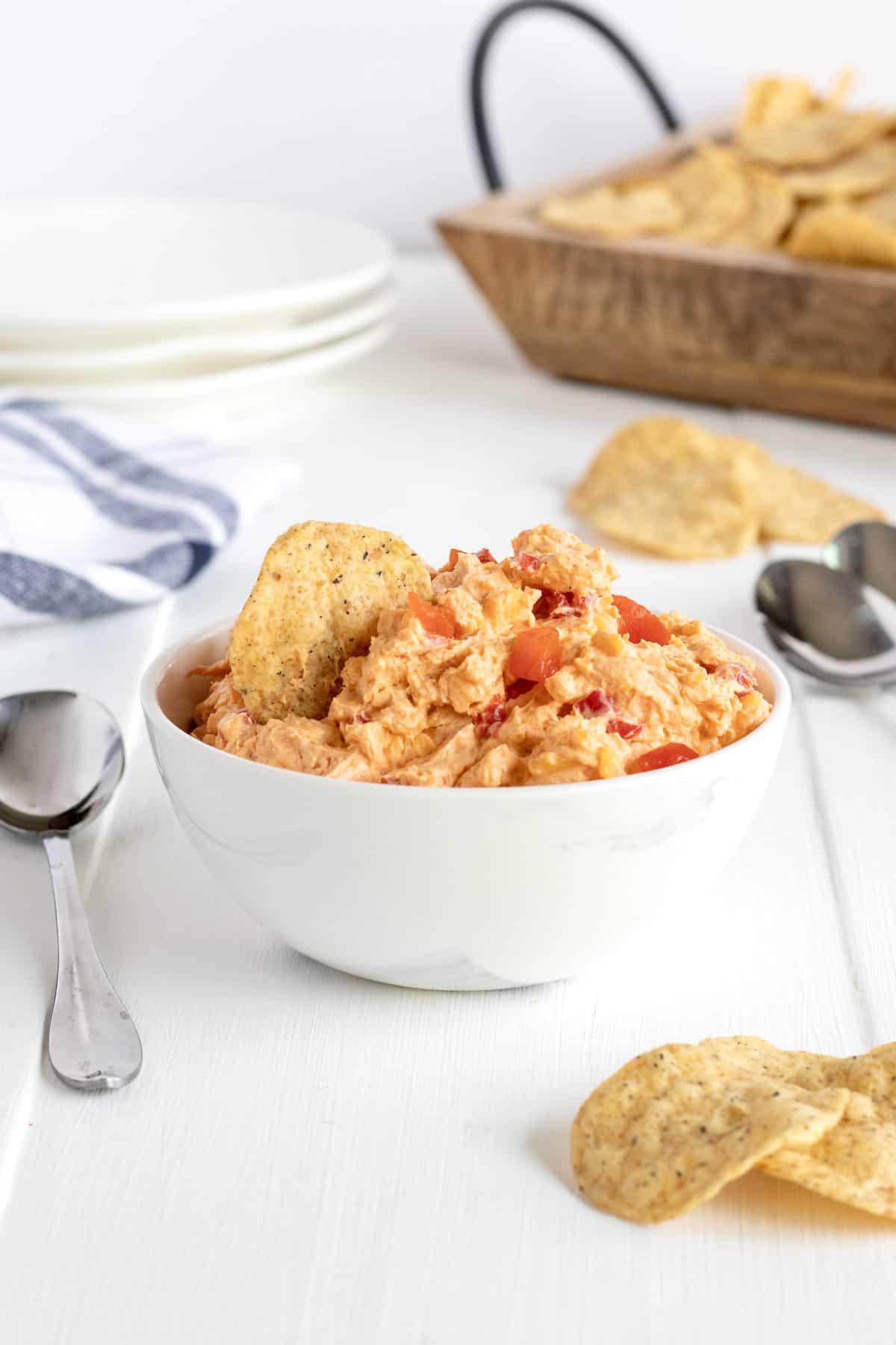 A white serving bowl with pimento cheese dip next to a spoon on a white counter.