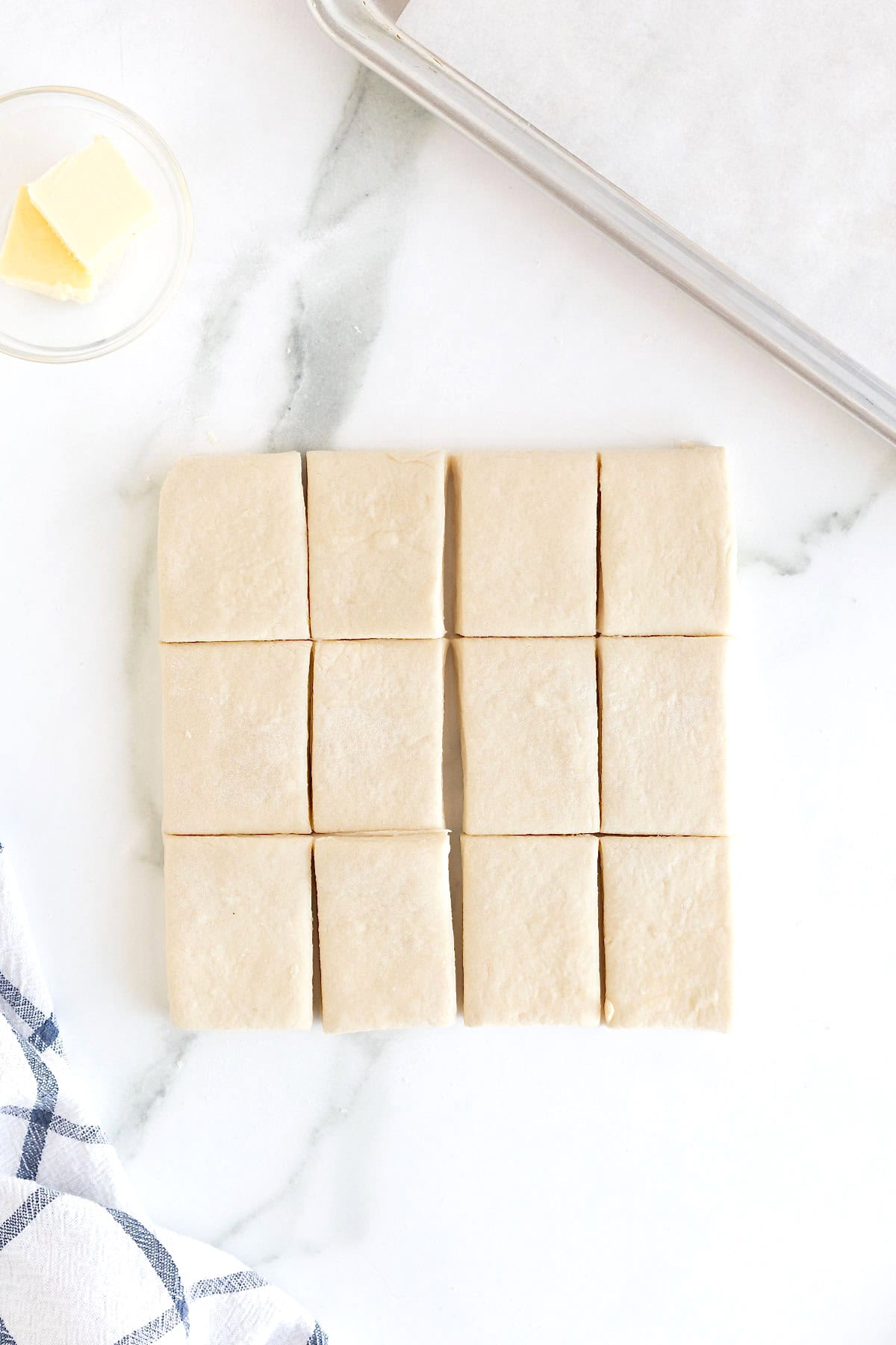 12 buttermilk biscuit dough squares on a floured white marble counter.