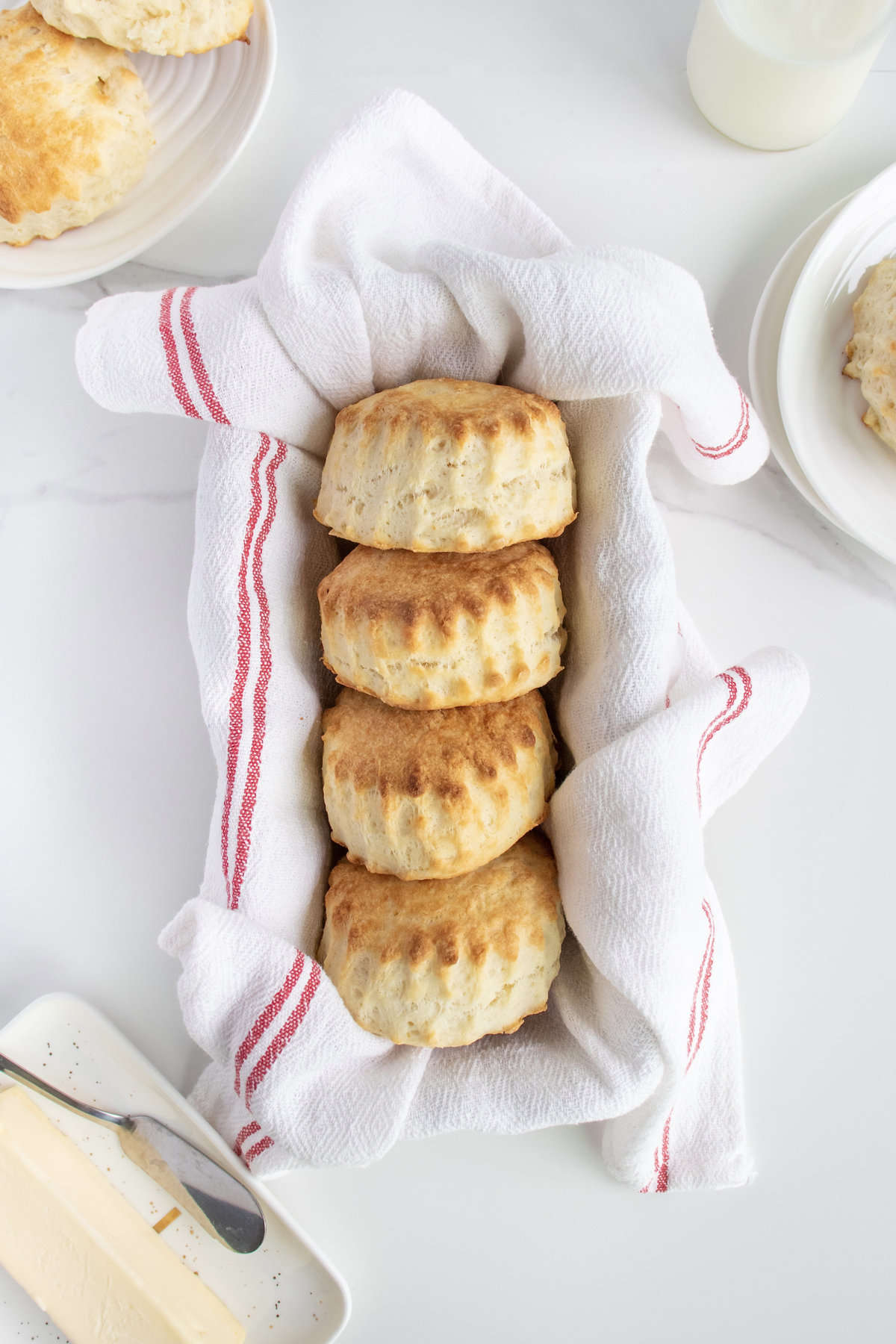 Four buttermilk biscuits in a rectangular serving dish lined with a white tea towel.
