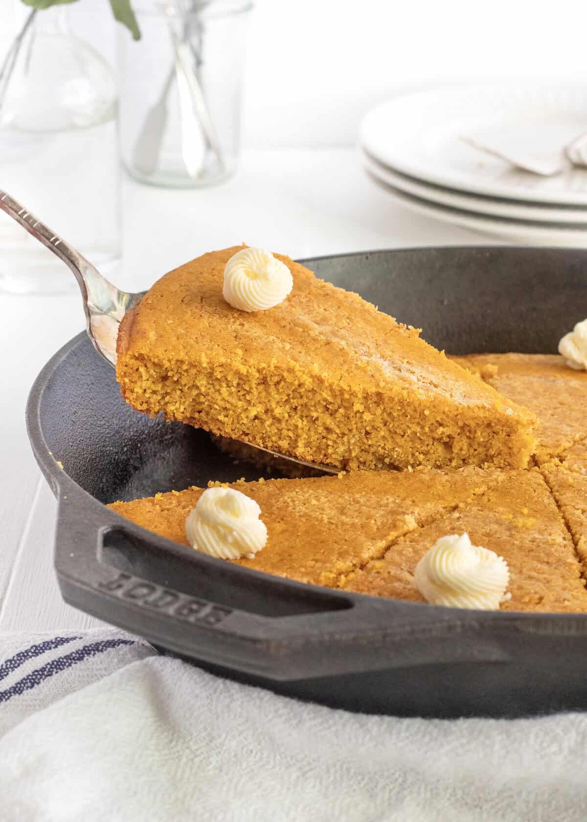 A slice of pumpkin cornbread being lifted from a cast iron skillet.