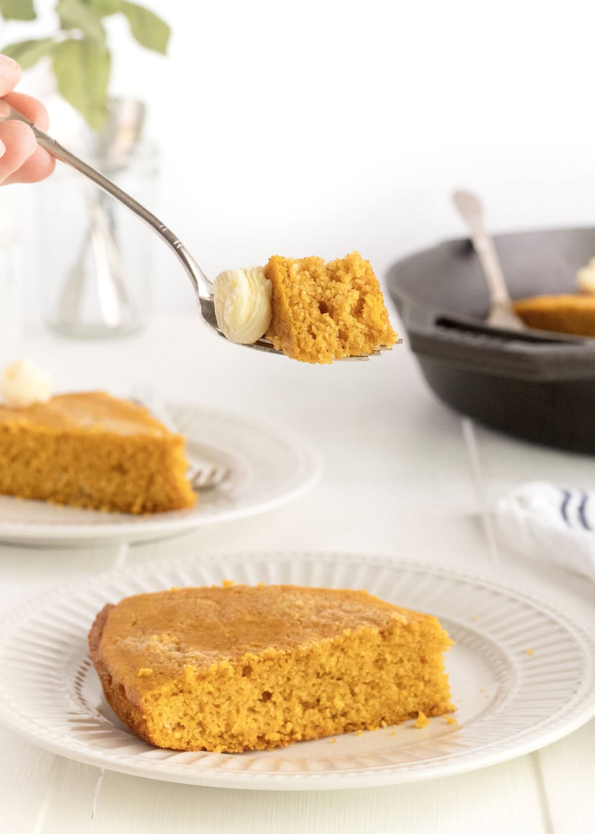 A fork holding a bite of pumpkin cornbread with a swirl of whipped butter on it.