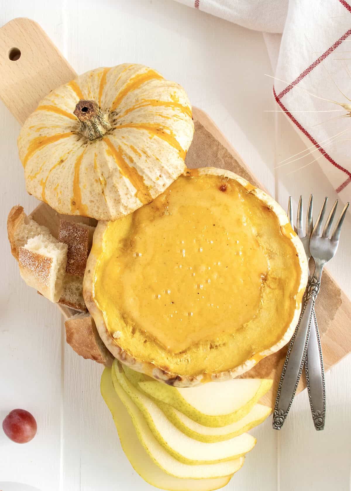 Fondue in a mini pumpkin shell on a light wood serving board.