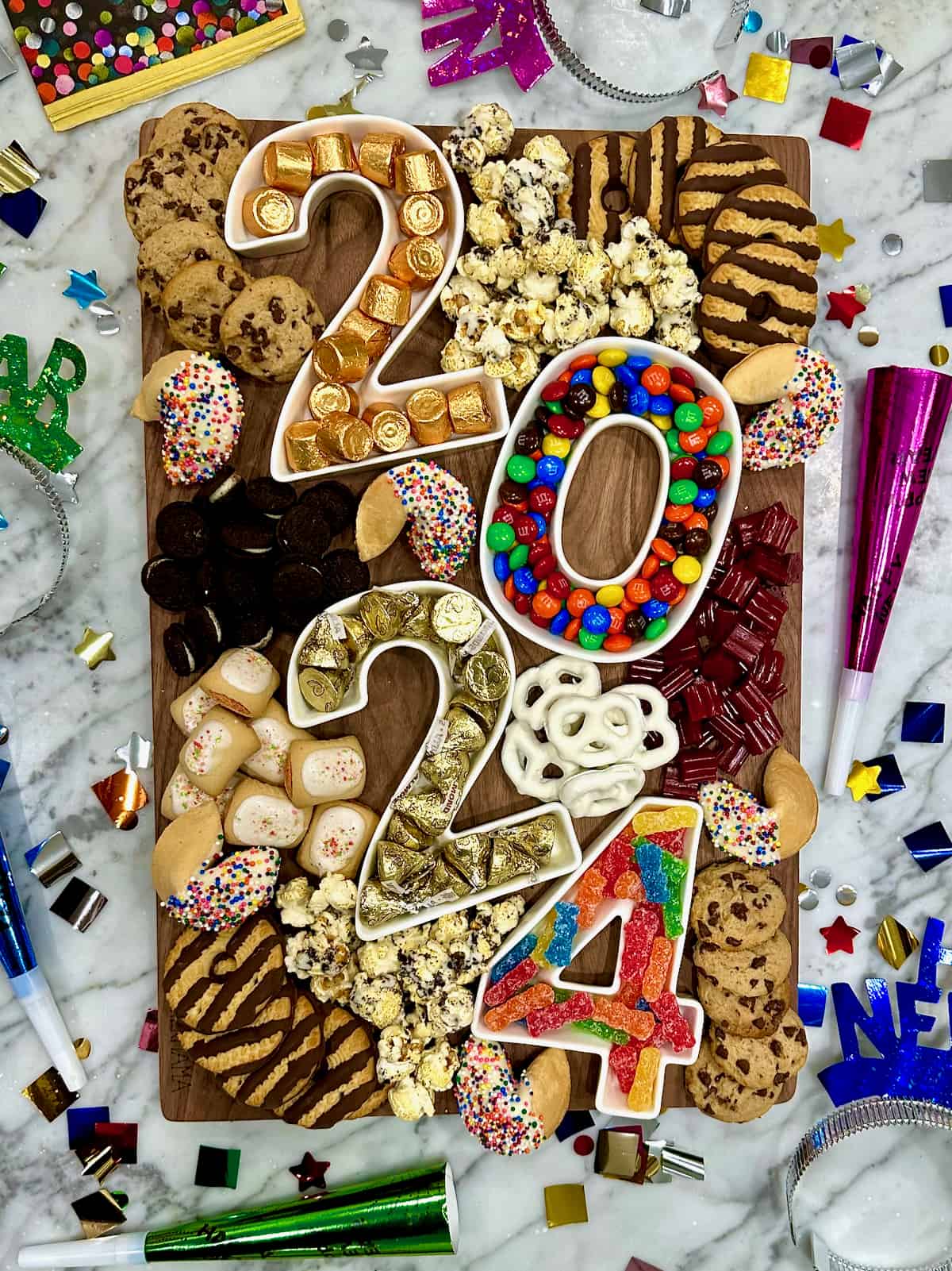 A dessert board with containers in the shapes of the numbers 2024 and candies and treats.