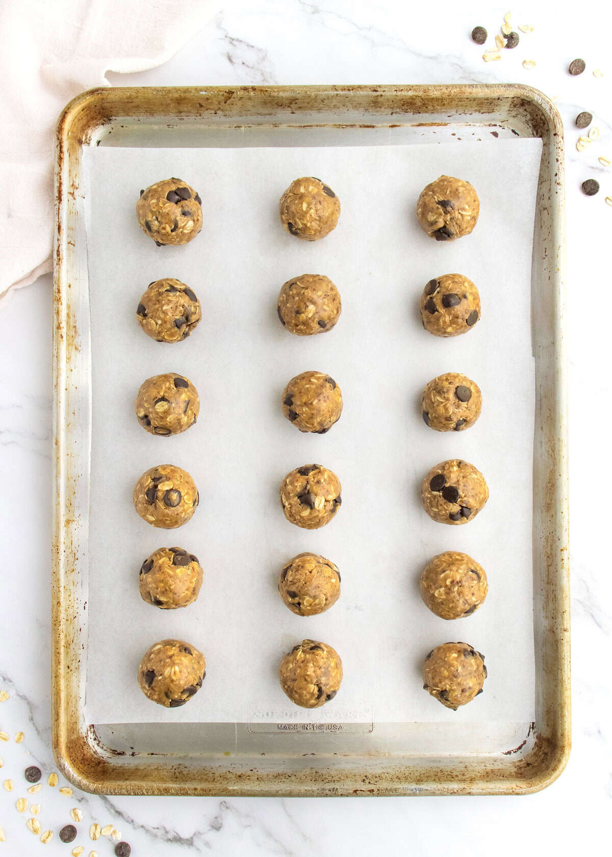 21 energy bites on a parchment lined aluminum baking sheet.