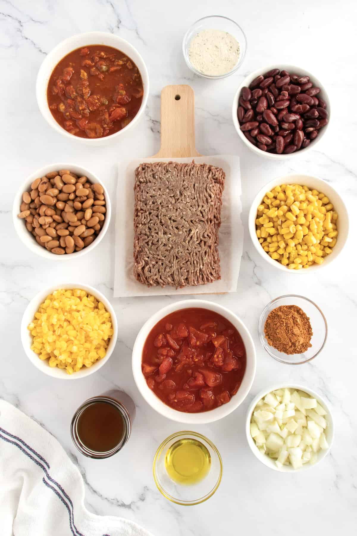 Ingredients for taco soup including ground beef, corn and beans, taco season ing, black beans, hominy and stewed tomatoes in glass dishes.