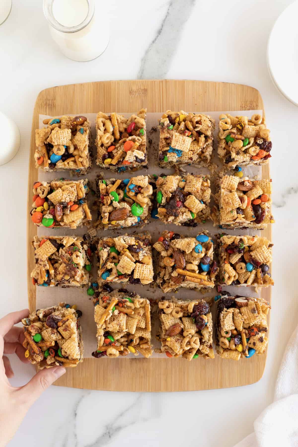 Snack bars made with cereal, pretzel sticks and M&M's on a wooden cutting board.