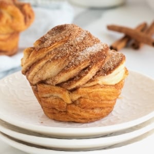 A cruffin with cinnamon sugar topping on a stack of white ceramic plates.