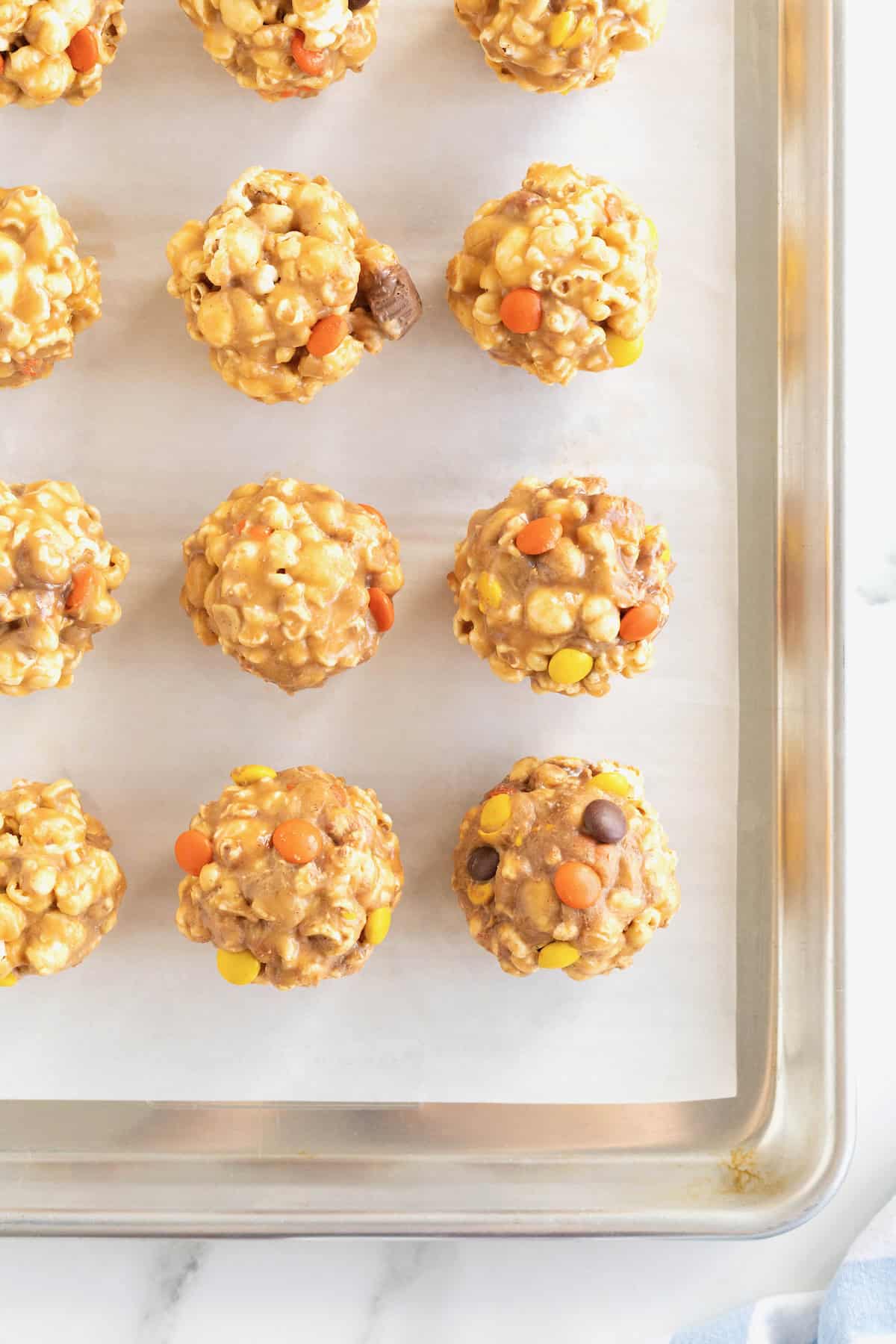 12 peanut butter popcorn balls on a parchment lined aluminum baking tray.