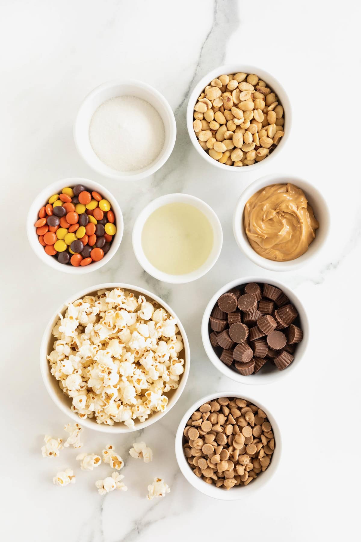 Ingredients for loaded peanut butter popcorn balls in small glass dishes a white marble counter.