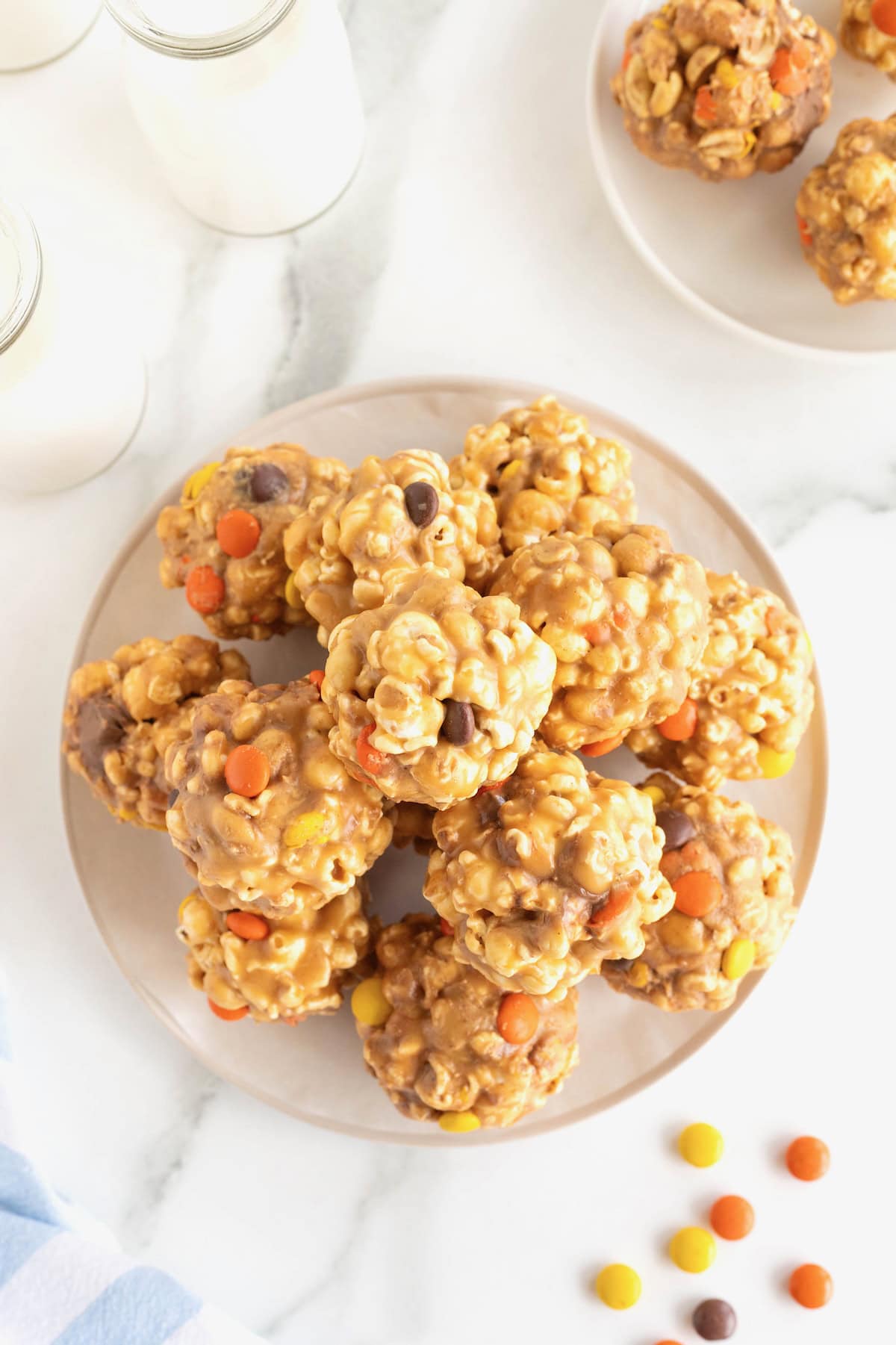 A round serving plate piled with loaded popcorn peanut butter balls on a white marble counter.