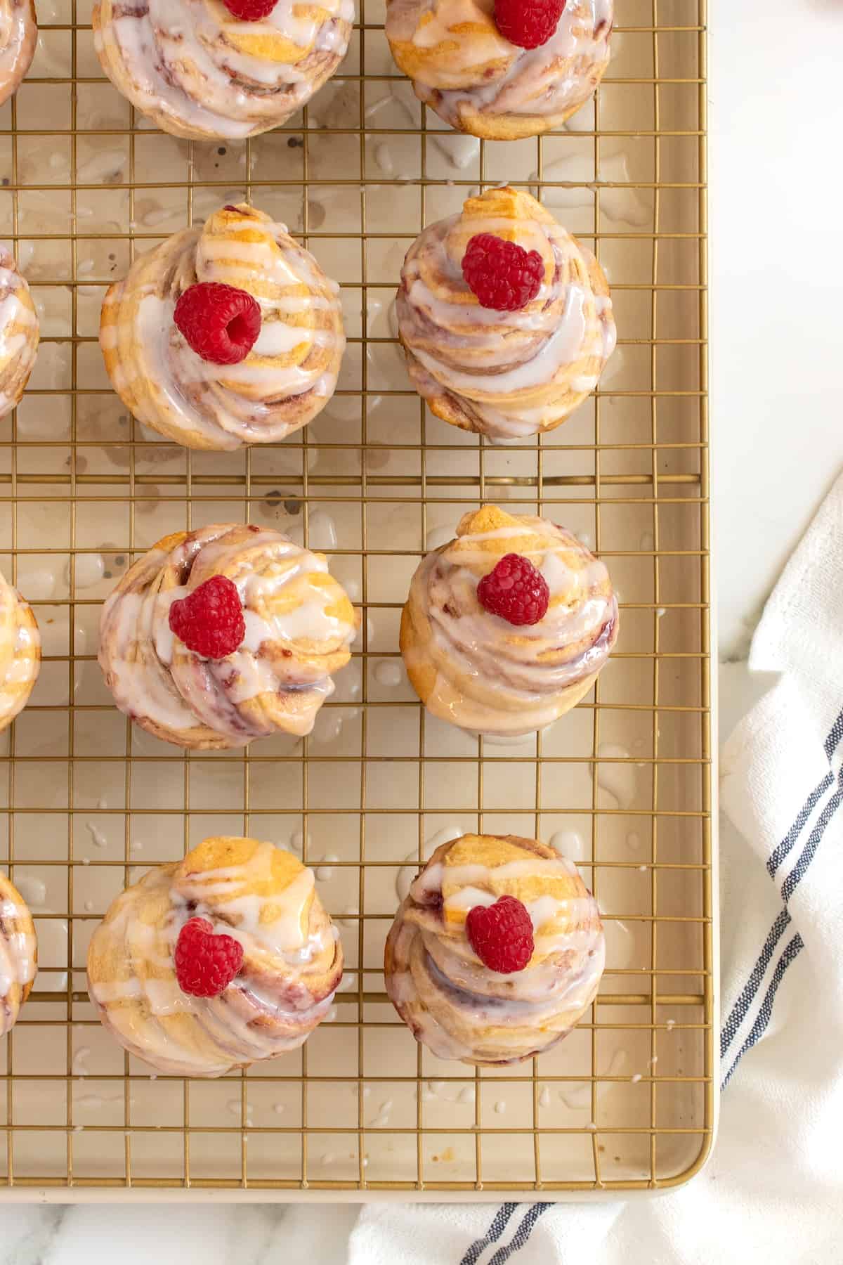 Cruffins topped with glaze and a fresh raspberry on a cooling rack.