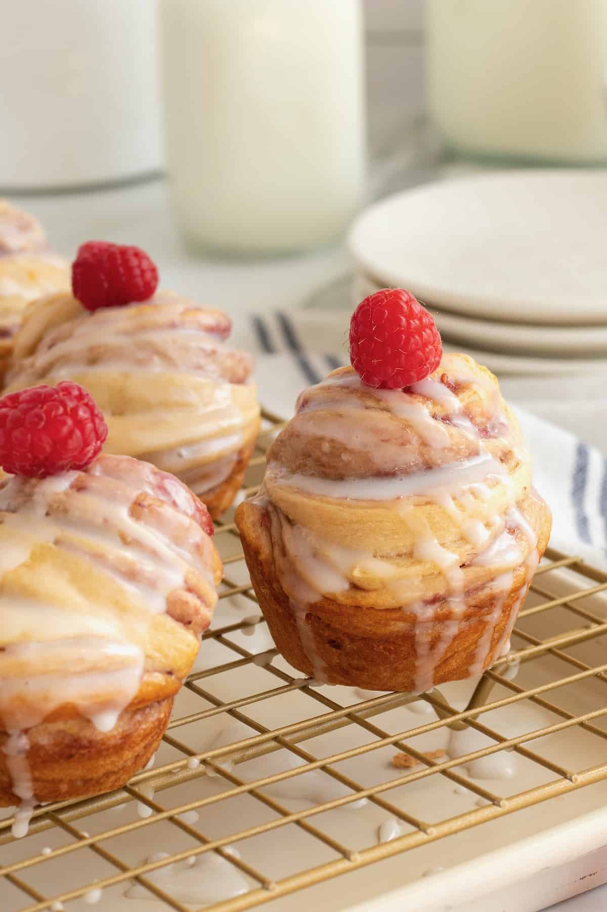 Cruffins topped with glaze and a fresh raspberry on a cooling rack.