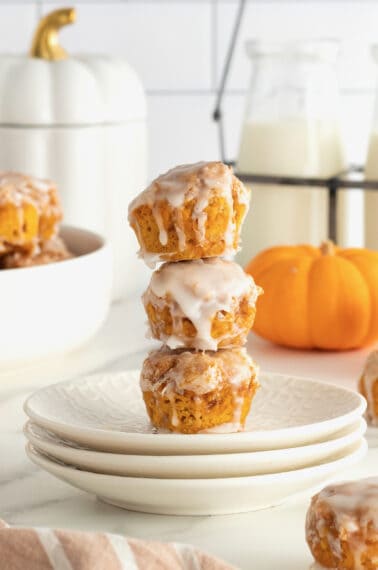 Three pumpkin fritters on a stack of white plates with a mini pumpkin in the background.