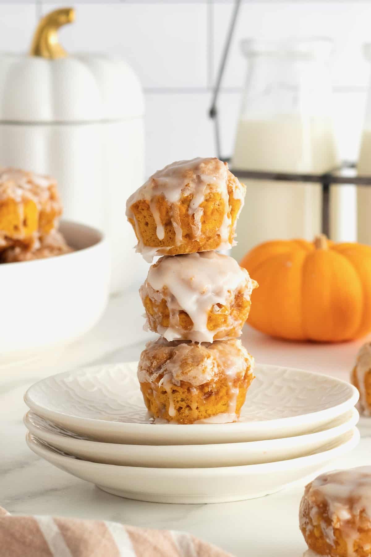 Three pumpkin fritters on a stack of white plates with a mini pumpkin in the background.