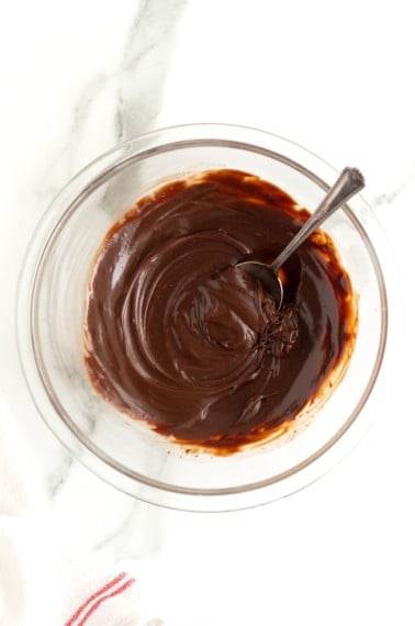 Chocolate ganache in a clear glass bowl with a metal spoon.