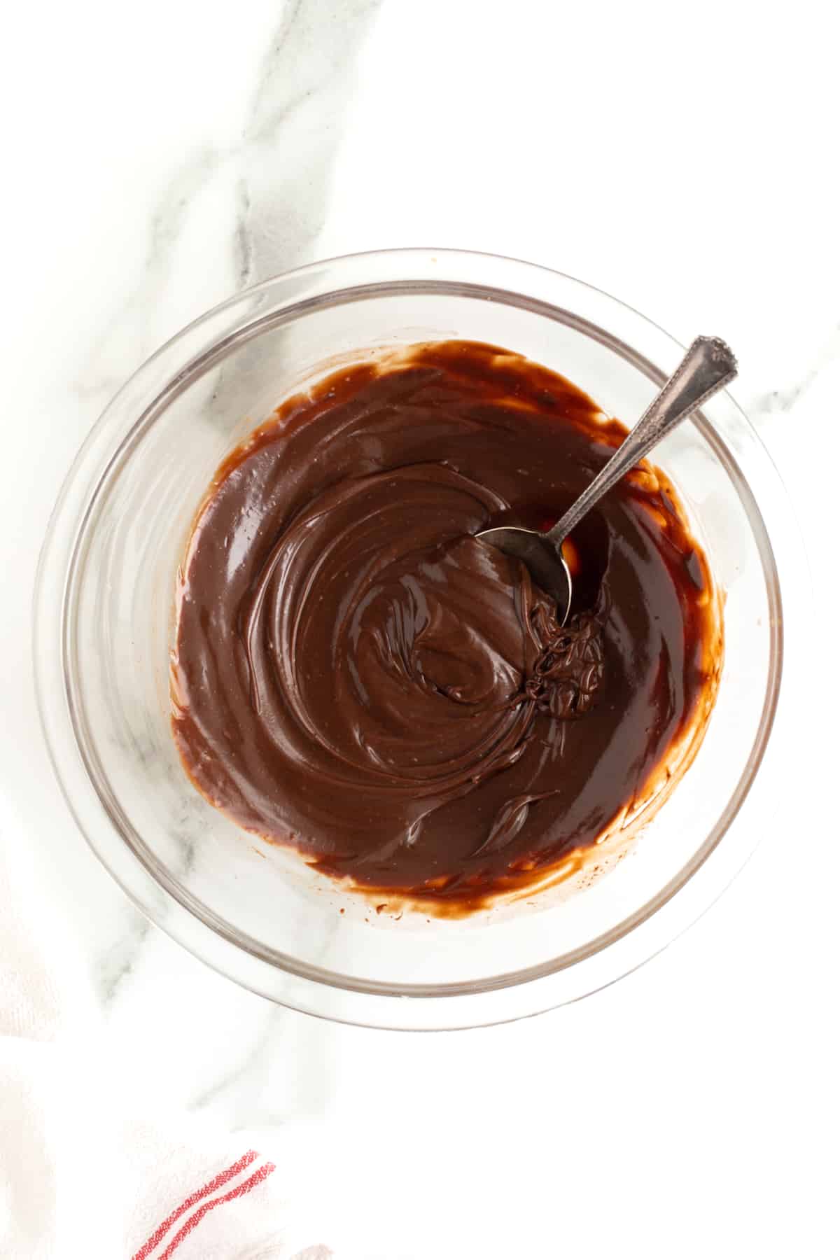 Chocolate ganache in a clear glass bowl with a metal spoon.