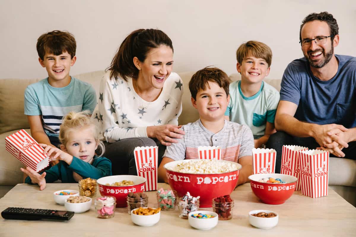 Family on the couch enjoying family movie night with popcorn and candy on table.