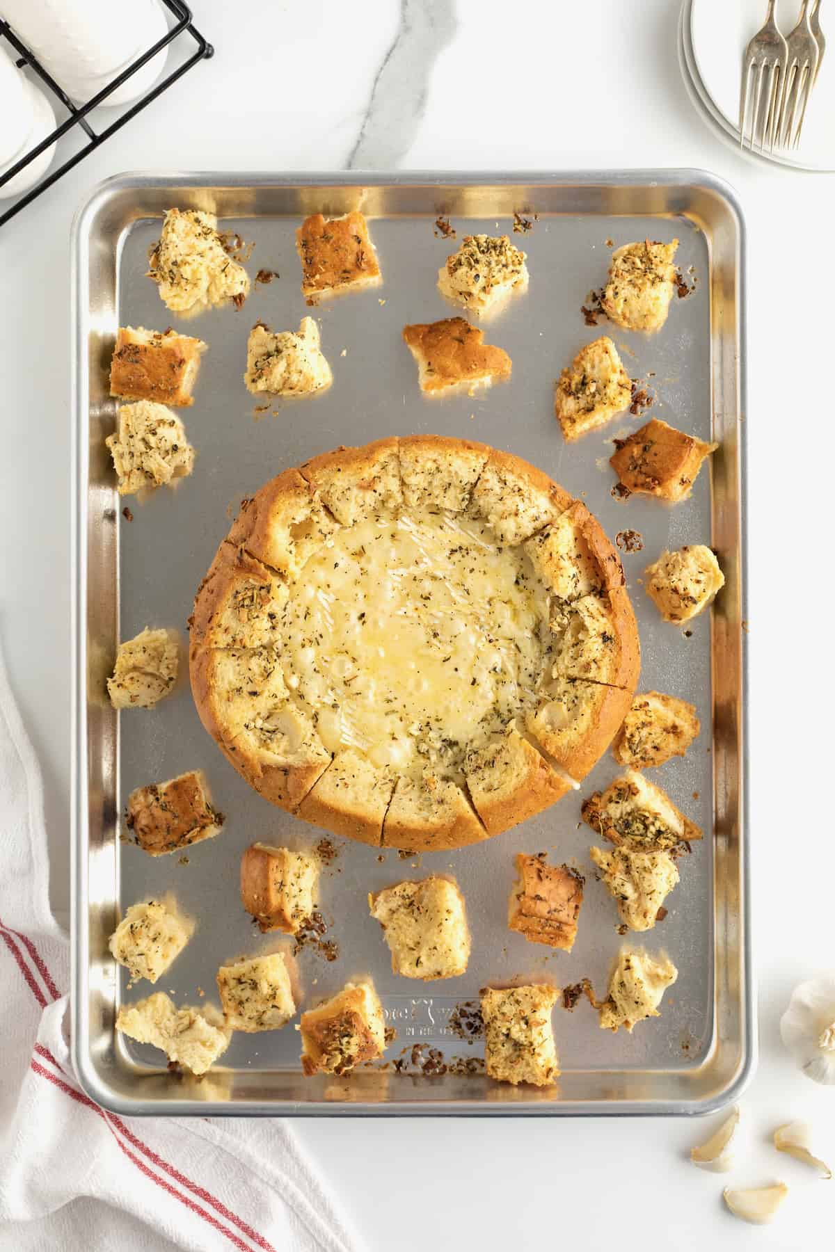 A baked bread bowl with wheel of brie inside arranged on baking sheet with bread chunks.