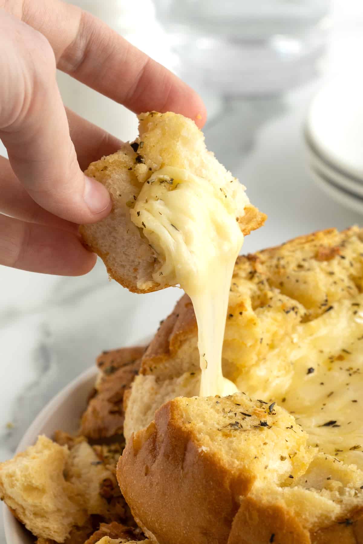 A hand holding a bread chunk dipped in melted brie.