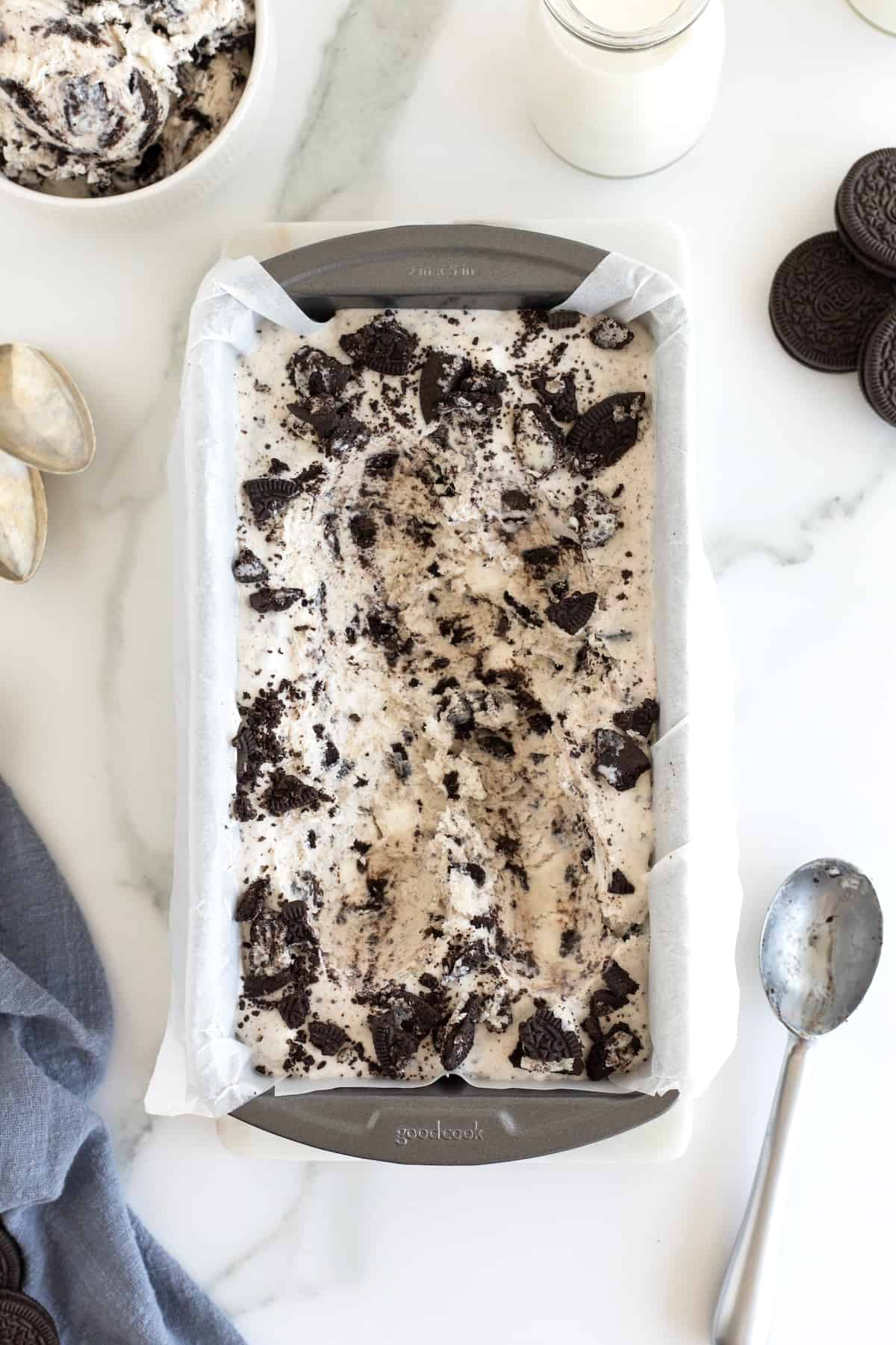 A metal spoon next to Cookies n' Cream ice cream in a loaf pan lined with parchment paper.