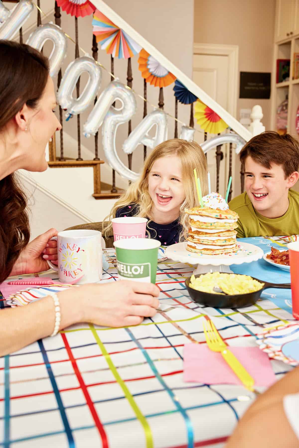 A family of a mother and four kids  enjoying breakfast on the first day of school with colorful hanging paper decorations in the background.