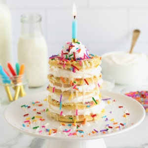 Five homemade pancakes with whipped topping between to make a layer cake, topped with whipped topping, sprinkles and a single candle.