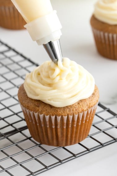 Cream cheese frosting piped onto a cupcake resting on a wire cooling rack.