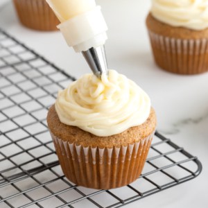 Cream cheese frosting piped onto a cupcake resting on a wire cooling rack.