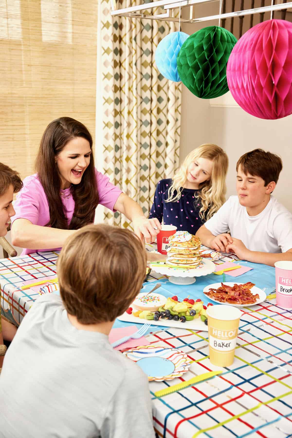 A family of a mother and four kids  enjoying breakfast on the first day of school with colorful hanging paper decorations in the background.