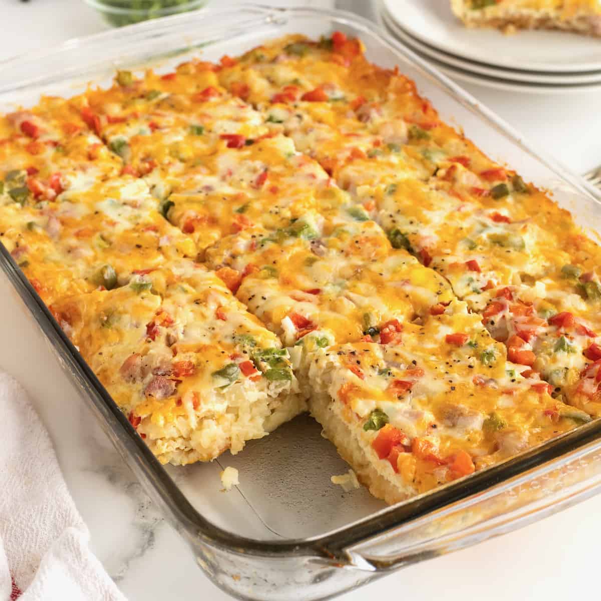 A clear glass baking dish with hash brown breakfast casserole with a slice cut out.