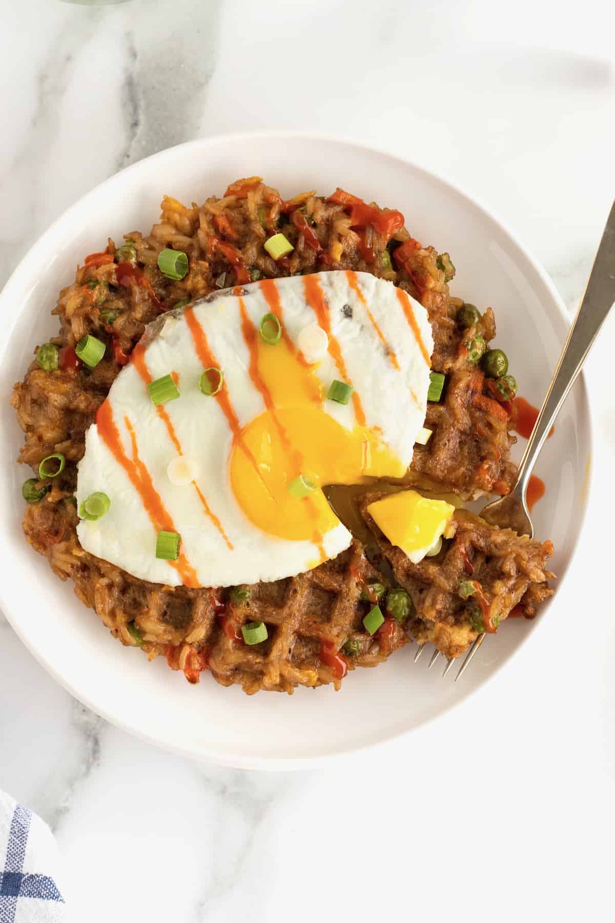 A fork with a bite of fried egg and leftover fried rice waffle.
