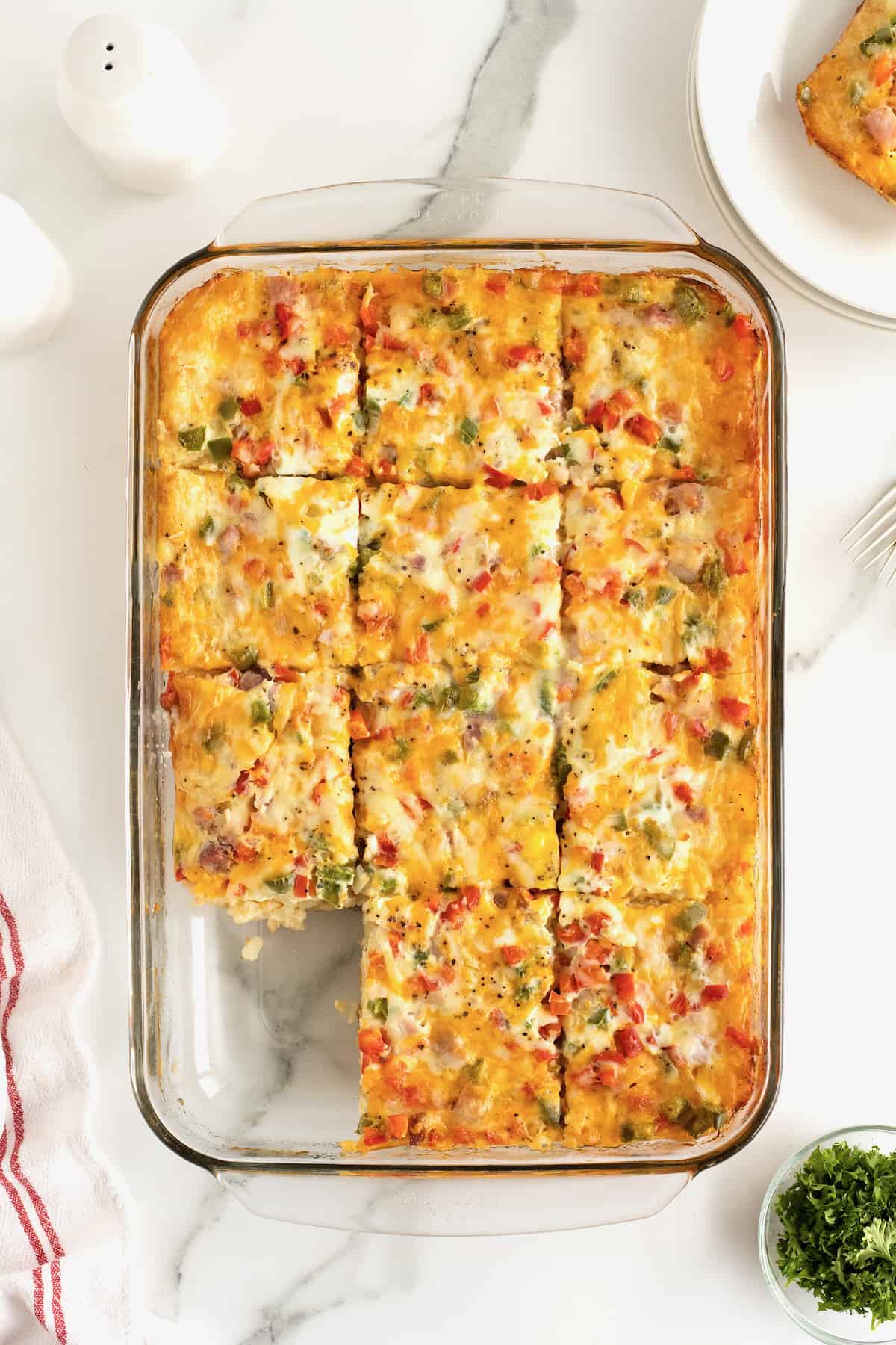 Cooked breakfast casserole in a glass casserole dish with a slice cut out of it.