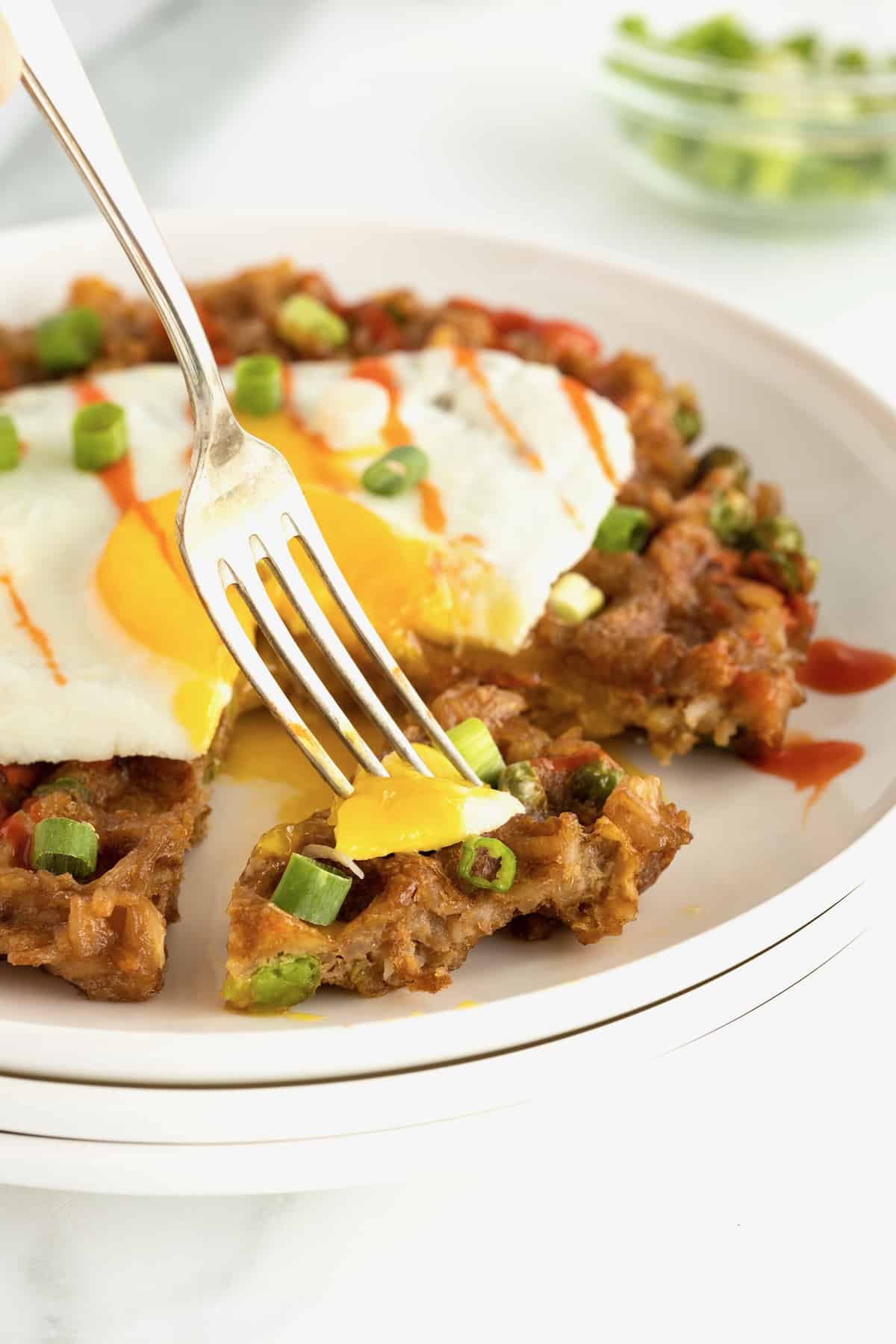 A fork with a bite of fried egg and leftover fried rice waffle.
