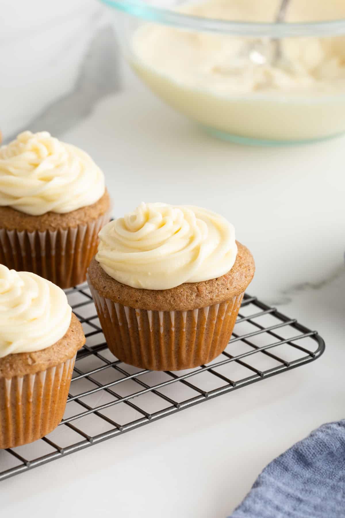 Three vanilla cupcakes with cream cheese frosting on a cooling rack.