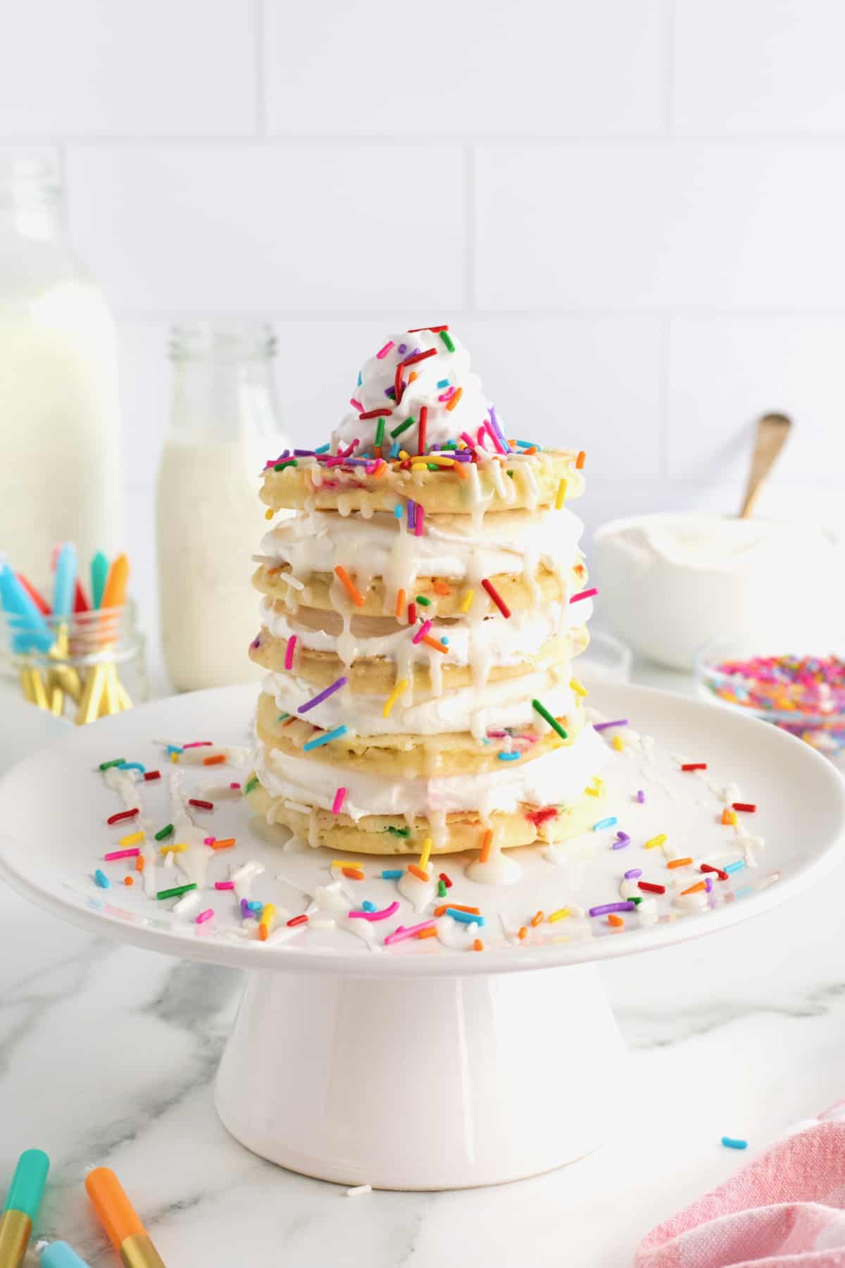 A layer cake made from confetti pancakes topped with whipped topping and rainbow sprinkles.