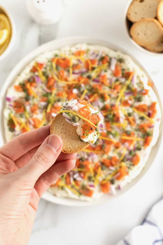 A round white serving platter with cream cheese smoked salmon dip and bagel chips.